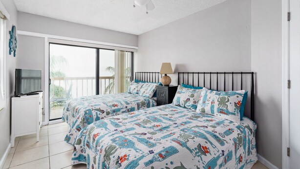 Une chambre avec deux lits, un ventilateur de plafond, une télévision et un balcon.
