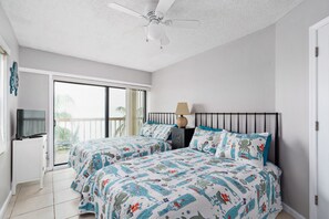 Une chambre avec deux lits, un ventilateur de plafond, une télévision et un balcon.