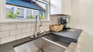 Een moderne keuken met een RVS spoelbak, een koffiezetapparaat en een rieten mandje op het aanrecht.