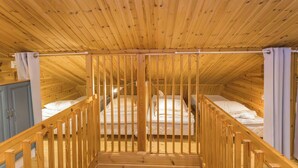 Un interior de madera con techo inclinado, una cama en el centro y una escalera que lleva a un nivel superior.