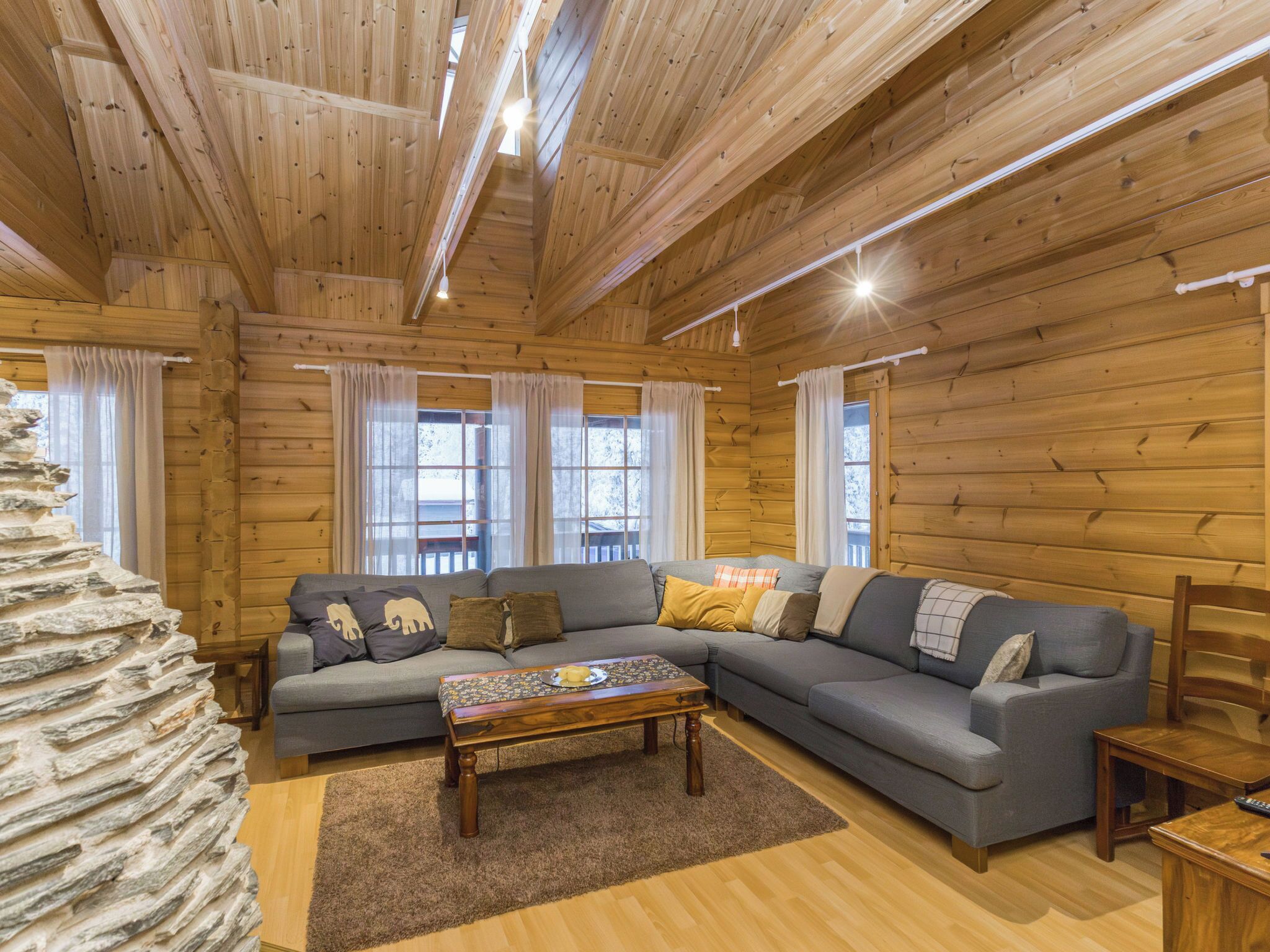 Un intérieur chaleureux d’une cabane en bois, avec un canapé d’angle, une table basse et un mur en pierre.