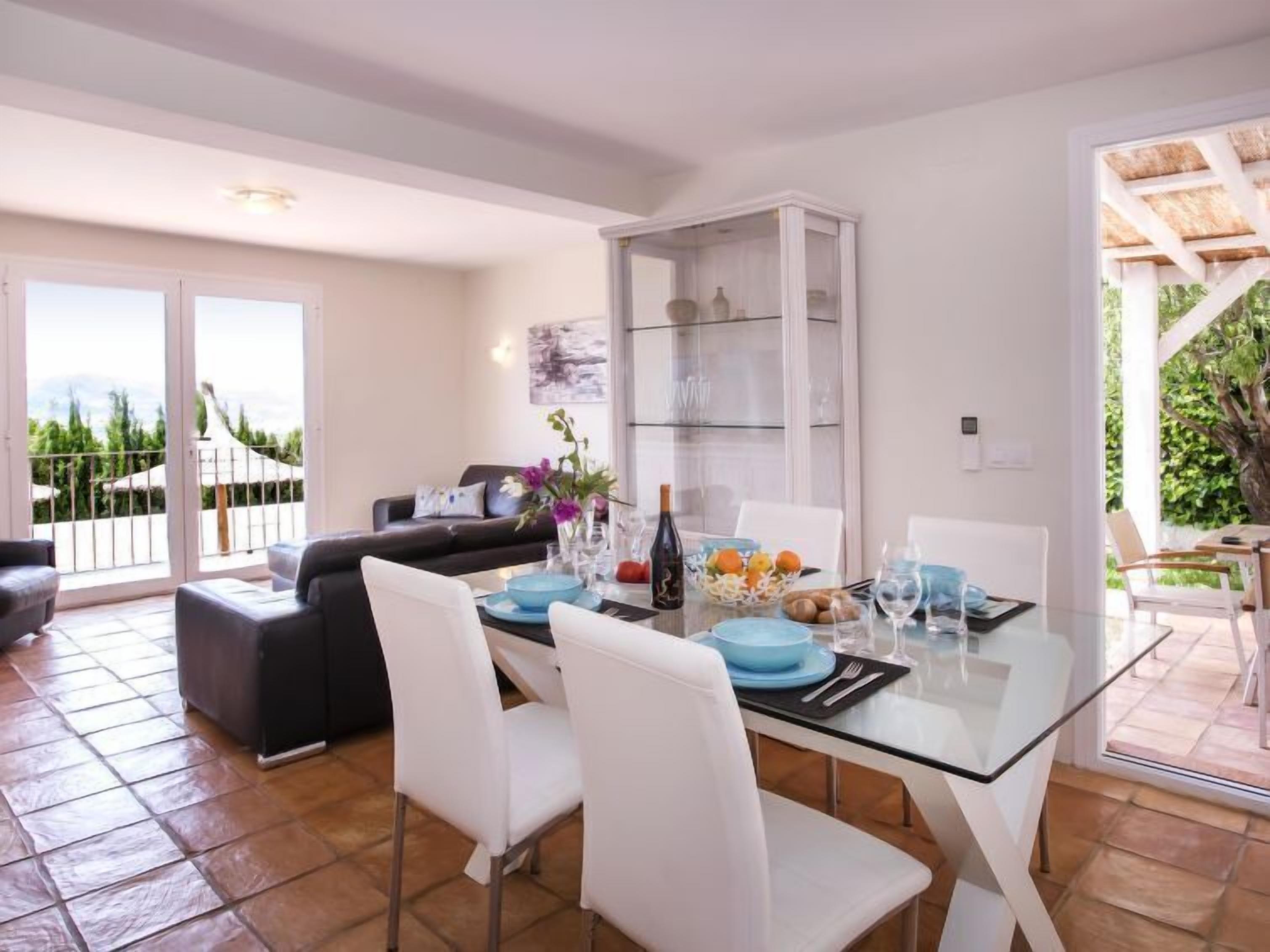 A dining area with a glass table, white chairs, and a black sofa.