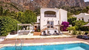 A modern pool area with a clear blue pool, lounge chairs, and a white building with a balcony. - Villa El Camino by Interhome (Jávea)