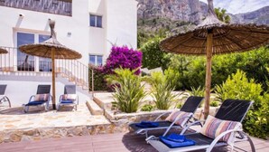 A sunlit outdoor area with lounge chairs and thatched umbrellas, surrounded by lush greenery and a mountainous backdrop. - Villa El Camino by Interhome (Jávea)