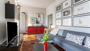A living room with a sofa, a coffee table with a vase of flowers, a flat-screen TV, a red cabinet, and framed artwork on the wall. - Vacation Apartment "Central Vista Lago" with Lake View & Private Terrace (Como)