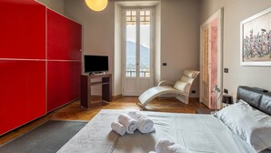 A bedroom with a bed, a TV, a chair, a painting, and a view through a window. - Vacation Apartment "Central Vista Lago" with Lake View & Private Terrace (Como)
