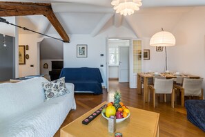 A cozy living room with a sofa, a dining table with chairs, a fruit bowl, and a ceiling fan.