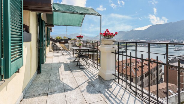 Une terrasse avec une table et des chaises, un auvent vert et une vue sur une rivière et des montagnes.