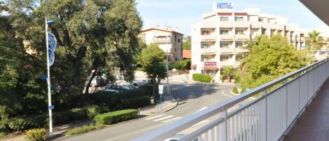 A hotel with a white facade and multiple balconies, surrounded by trees and parked cars.