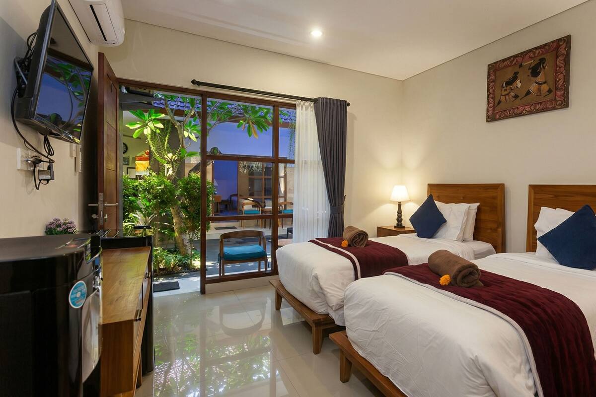 A hotel room with two beds, a TV, and a balcony with plants.