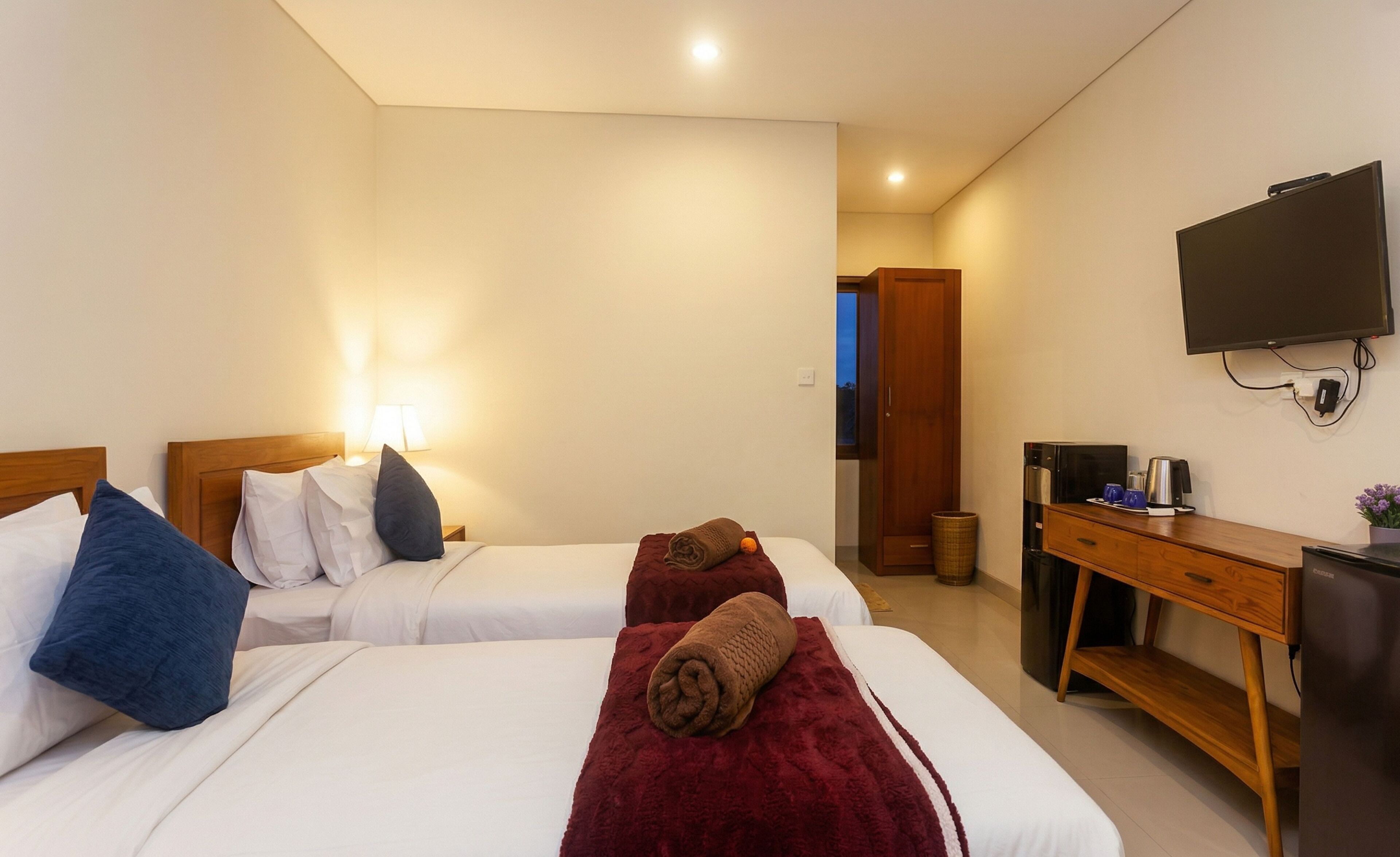 Una habitación de hotel con dos camas, televisión, escritorio y un cesto de basura.