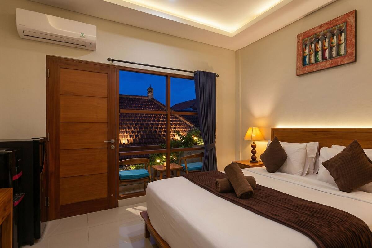 A hotel room with a bed, bedside table, lamp, and a painting on the wall.