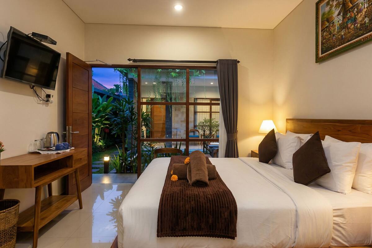 A hotel room with a bed, a desk, a TV, and a view of a garden.
