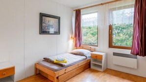 A bedroom with a wooden bed, a nightstand, a bedside table, a framed picture on the wall, and a window with curtains. - Vacation home Měřín by Interhome (Slapy)