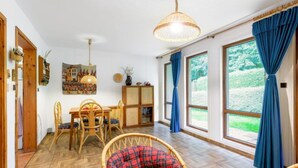 A spacious room with a dining area, a wicker chair, and large windows with curtains. - Vacation home Měřín by Interhome (Slapy)