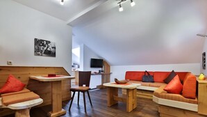 A modern interior with a wooden dining table, a sofa with orange cushions, and a television mounted on the wall.