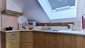 A compact kitchen with wooden cabinets, a microwave, a kettle, and a window above the sink.