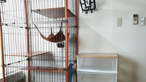 A pet cage with a brown hammock, a clear plastic storage unit, and a wall-mounted light fixture. - Cote House (Osaka)