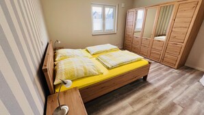 Quarto com cama de madeira, roupa de cama amarela, luminária de cabeceira, janela e guarda-roupa de madeira.