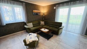 A living room with a green sofa, a small table with a decorative item, a bench with a blanket, and a painting on the wall.