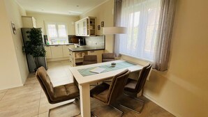 Cozinha compacta com área de refeições, destacando uma mesa com cadeiras, geladeira, armários e uma janela com cortinas.