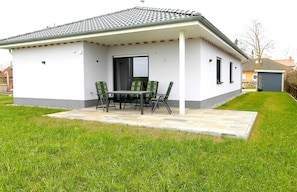 A modern house with a covered patio, a dining table with chairs, and a well-maintained lawn.