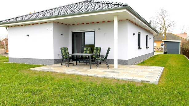 Uma casa moderna com alpendre coberto, mesa de jantar com cadeiras e gramado bem cuidado.