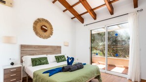 A bedroom with a wooden headboard, a green bedspread, and a view of the outdoors through a sliding glass door. - Villa Flomertor 2  (Ciutadella de Menorca)