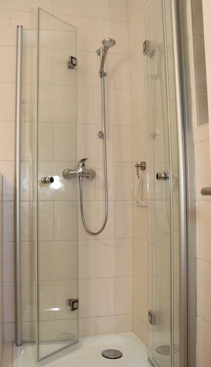 Une cabine de douche fermée par des parois en verre, dotée d’un pommeau de douche à main et d’un robinet fixé au mur.
