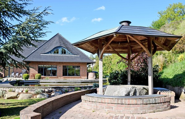 A brick house with a sloped roof and a wooden gazebo in a landscaped garden.