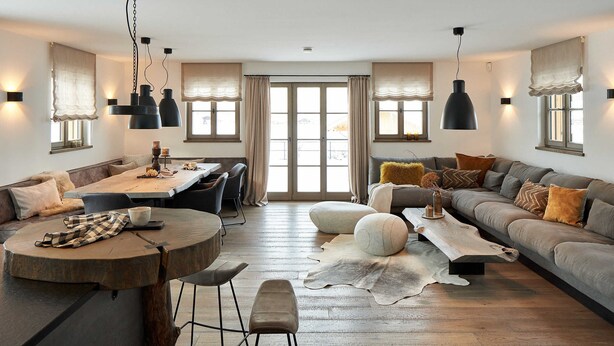 A spacious living area with a wooden dining table, a sofa, and a large window with curtains. - Chalet Hirschbergblick (Rottach-Egern)