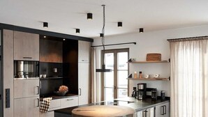 A modern kitchen with a central island, bar stools, and a pendant light. - Chalet Hirschbergblick (Rottach-Egern)