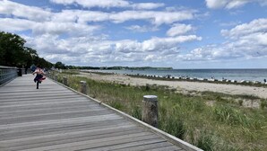 A wooden boardwalk leading to a beach with a clear sky and distant land. - Haffblick Whg. Ha16, Deutschland (Ostseebad Boltenhagen)