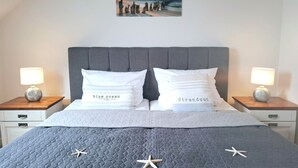 A bed with a grey quilt, two white pillows with text, starfish decorations, and a painting above. - Haffblick Whg. Ha16, Deutschland (Ostseebad Boltenhagen)