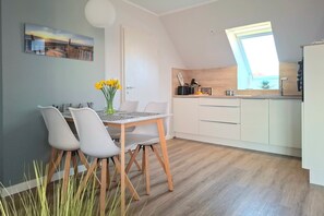 Une cuisine moderne avec des meubles blancs, une table à manger en bois et quatre chaises, et une fenêtre au-dessus de l’évier.