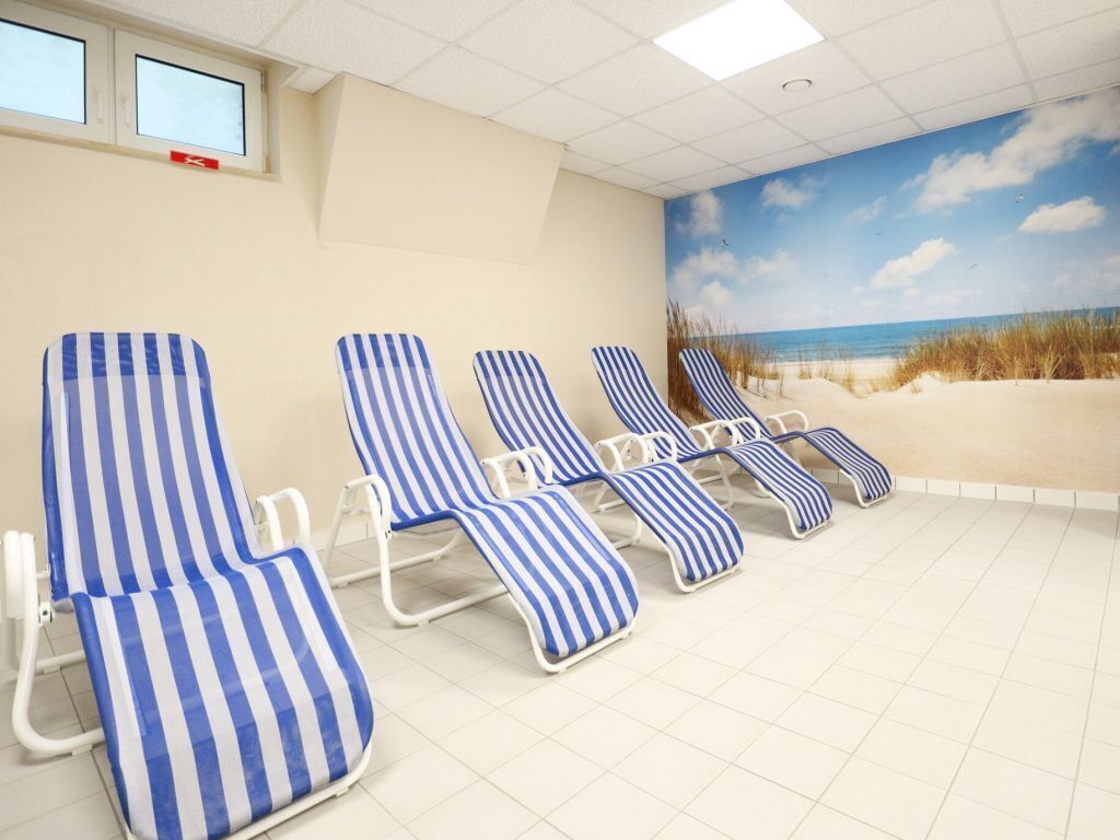 A room with four striped lounge chairs, a beach mural on the wall, and a tiled floor.