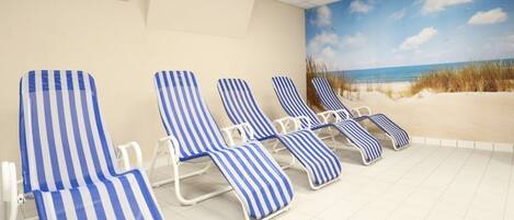 A room with four striped lounge chairs, a beach mural on the wall, and a tiled floor.