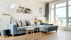 A modern living room with a grey sofa, a round coffee table, and a large window with a view. - Haffblick Whg. Ha16, Deutschland (Ostseebad Boltenhagen)