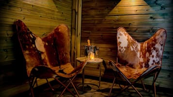 A cozy room with wooden walls, two leather chairs, a small table with a candle, and a bottle.