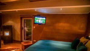 Ein Hotelzimmer mit Bett, Wandfernseher, kleinem Tisch und einer Tür zu einem weiteren Raum.