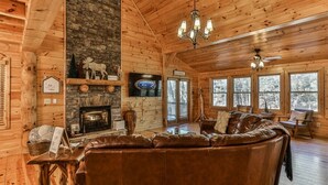 A log cabin interior with a fireplace, leather sofa, and large windows. - Nice & Knotty On The River | Ellijay, GA (Ellijay)