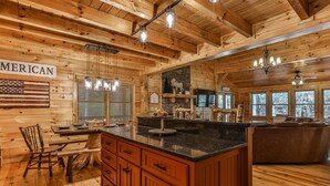 A wooden cabin interior with a kitchen island, wooden cabinets, and a dining table. - Nice & Knotty On The River | Ellijay, GA (Ellijay)