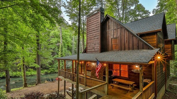 A cabin with a deck, a fireplace, and a view of a river. - Nice & Knotty On The River | Ellijay, GA (Ellijay)