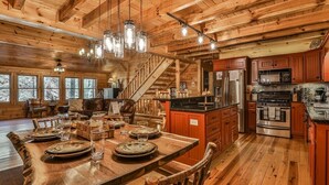 A wooden cabin interior with a dining area, kitchen, and staircase. - Nice & Knotty On The River | Ellijay, GA (Ellijay)