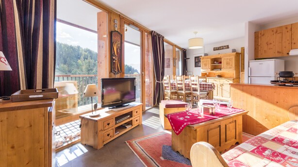 Une pièce confortable avec une télévision, des meubles en bois, un coin repas et une cuisine.