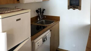 Une cuisine compacte avec des meubles de rangement en bois, une cuisinière encastrée, un évier et un lave-vaisselle.