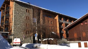 Un immeuble à plusieurs étages, doté de murs extérieurs en pierre et en bois, d’un toit enneigé et d’une enseigne indiquant un centre de sports d’hiver.