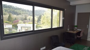 Une chambre avec une grande fenêtre, un bureau, une chaise et un lit.