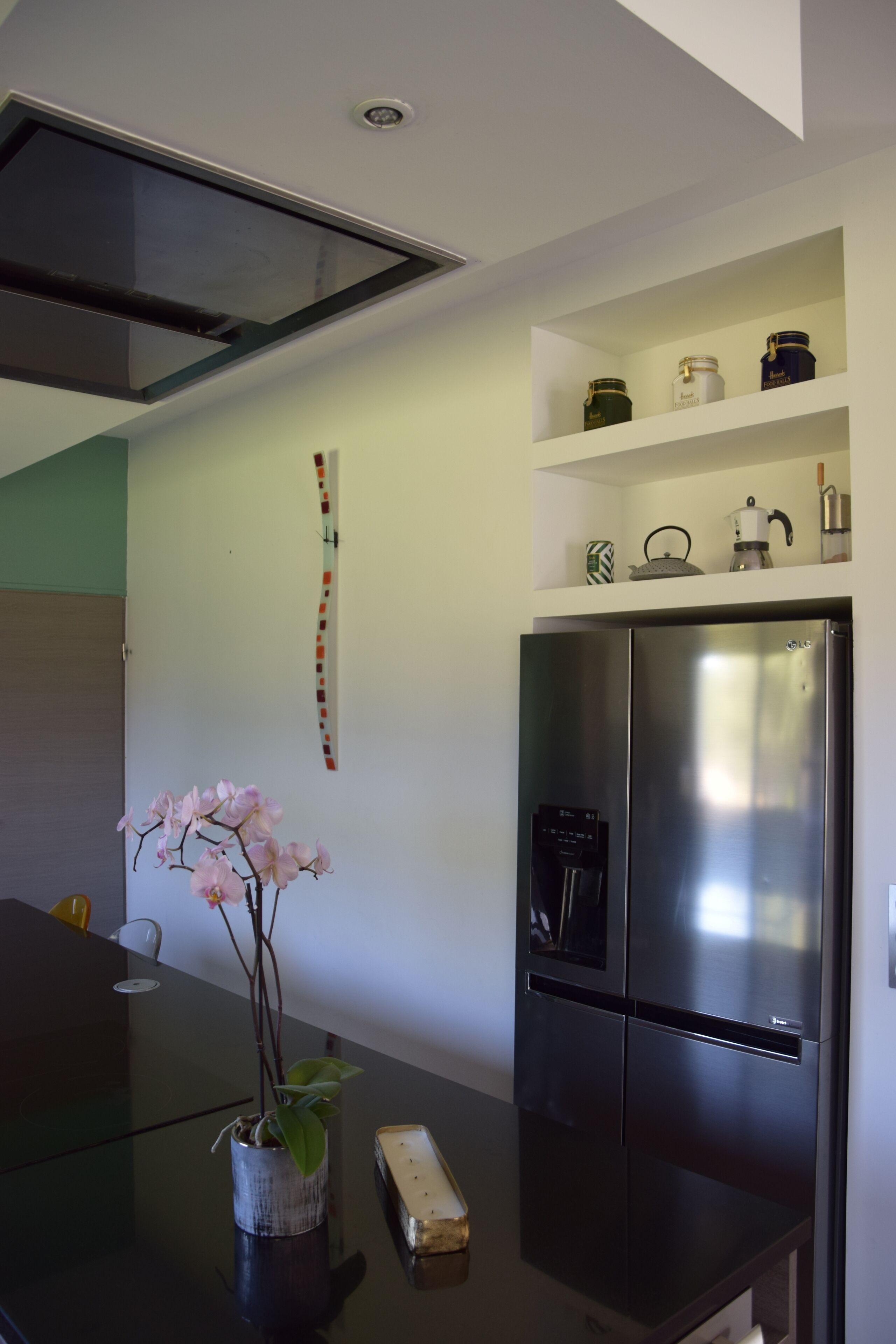 Une cuisine moderne avec un réfrigérateur en acier inoxydable, une table à manger avec un plateau en verre et une orchidée en pot.