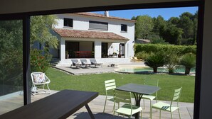 Une maison moderne dotée d’un patio, d’une piscine et offrant une vue sur la verdure environnante.
